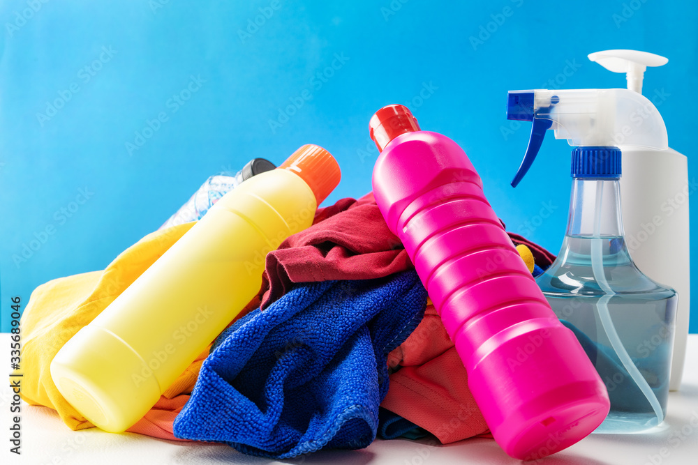 Plastic bottles of cleaning products set with pile clothes on white table blue background.