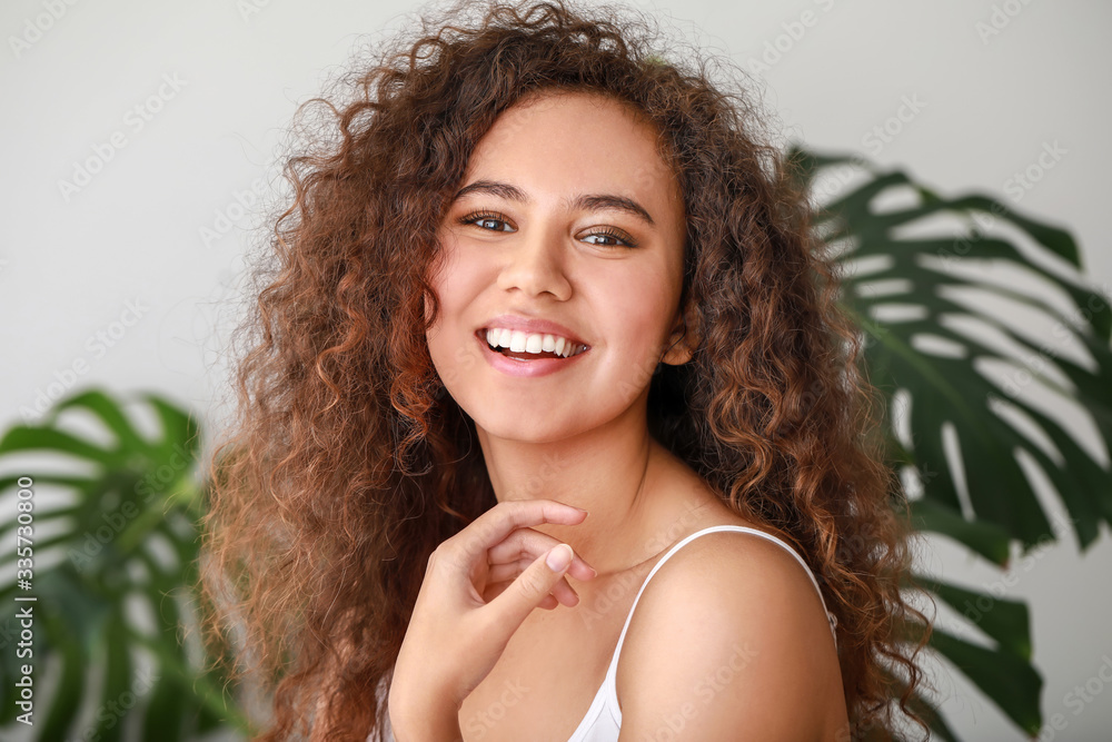 Beautiful young African-American woman with healthy skin and tropical leaves on light background