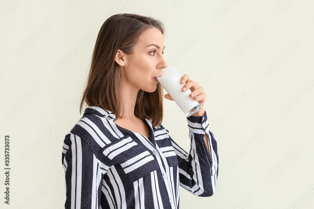 Beautiful young woman with glass of milk on light background