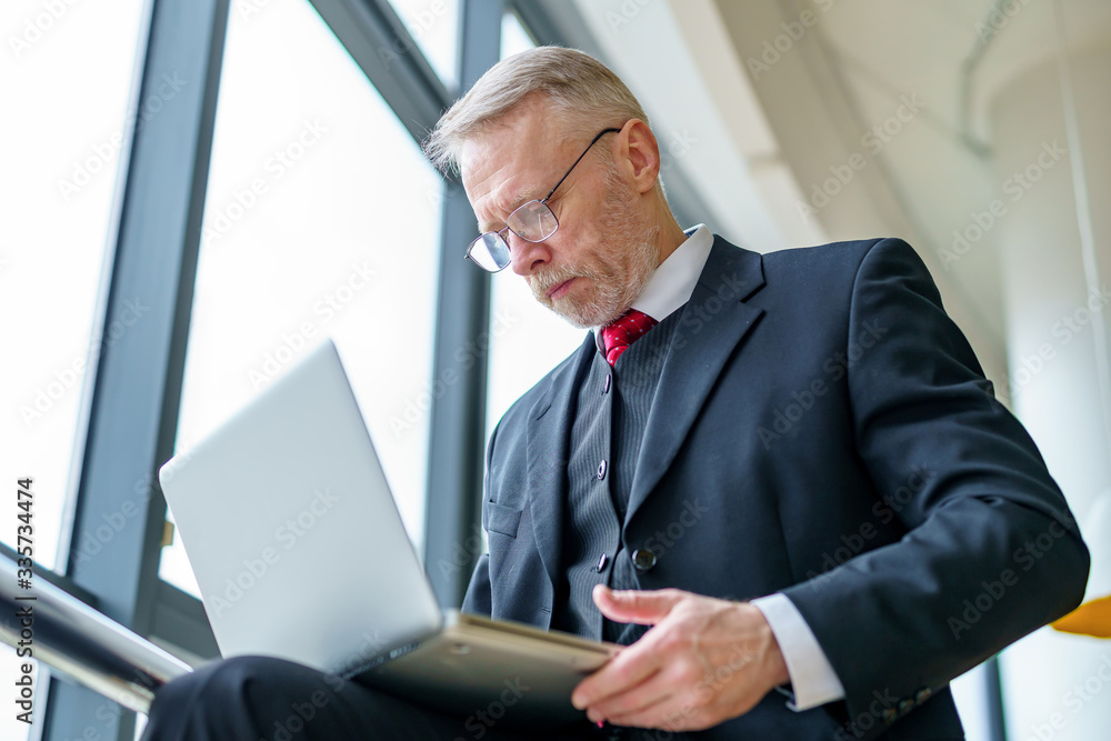 Senior businessman near the panoramic window. Speaking with colleagueas over the laptop. Videoconfer