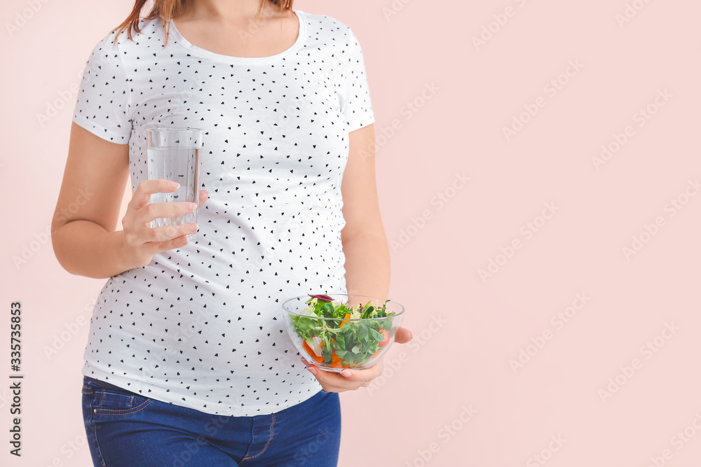 Beautiful pregnant woman with healthy salad and water on color background