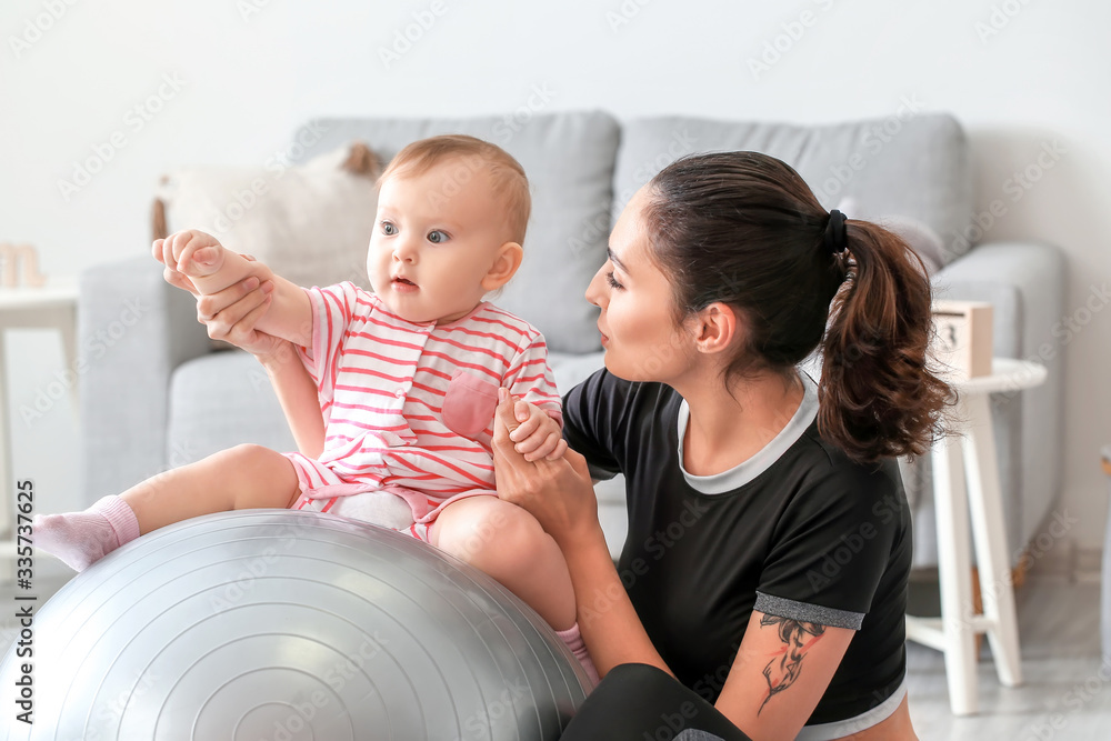 Young sporty mother and her baby doing exercises with fitball at home