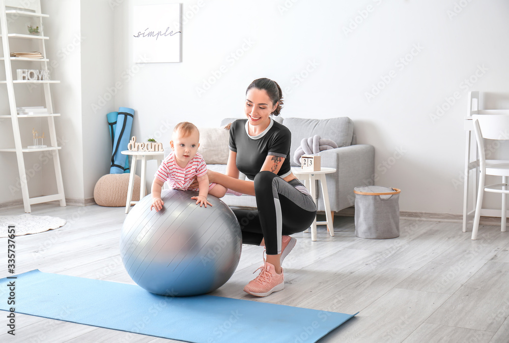 Young sporty mother and her baby doing exercises with fitball at home