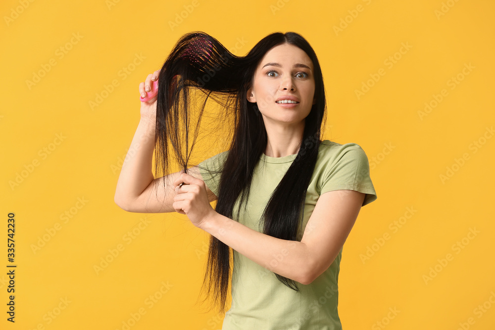 Beautiful young woman brushing hair against color background