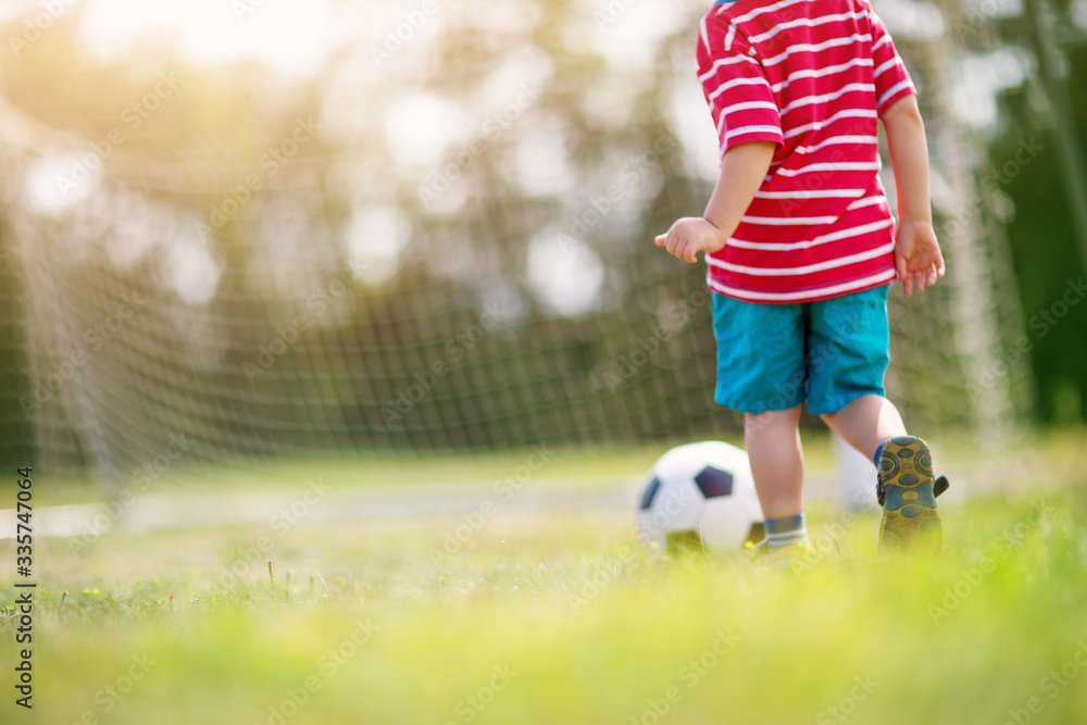 Little boy playting football on the field with gates