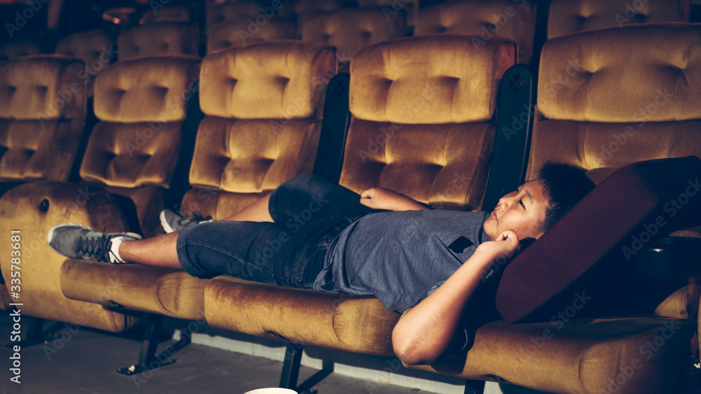 A boy laying down on the armchair and enjoy watching movie in cinema.