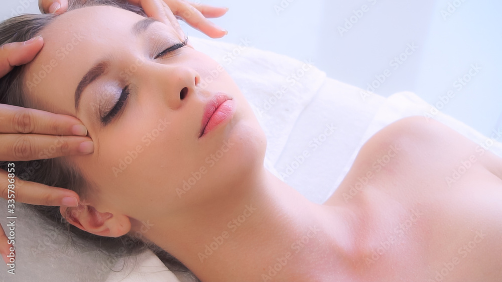 Relaxed woman lying on spa bed for facial and head massage spa treatment by massage therapist in a l