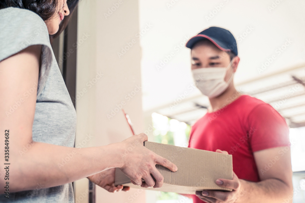 Asian postman or deliveryman carry small box deliver to young woman customer in front of door at hom