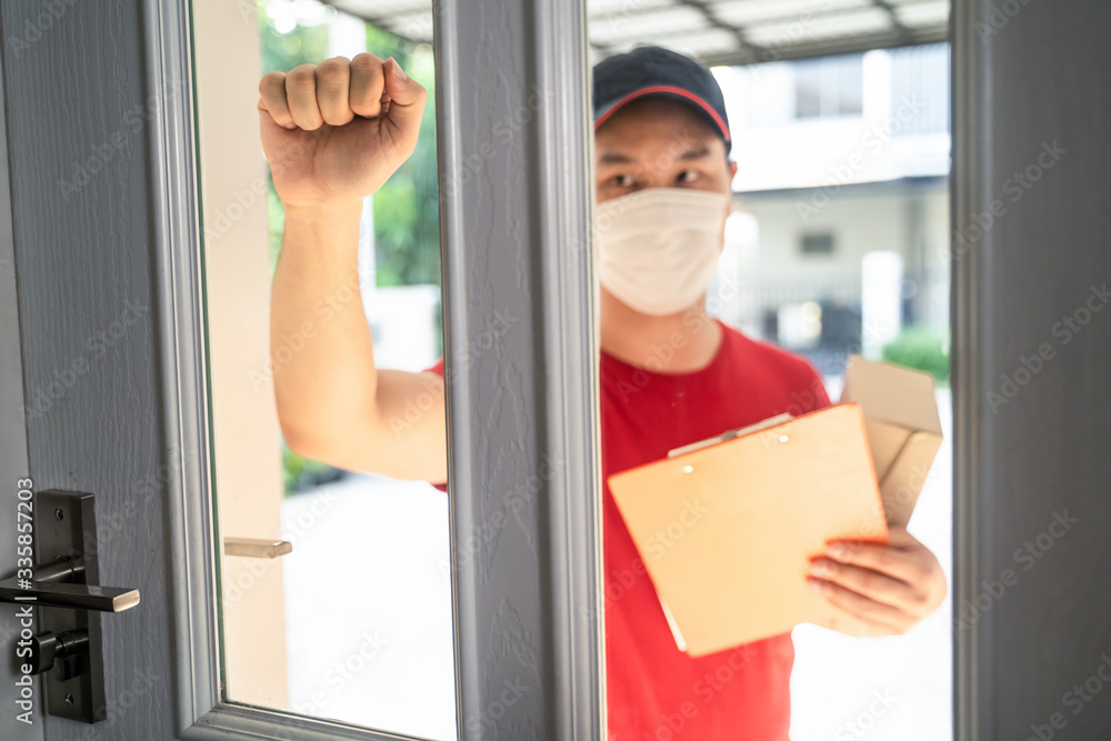 Asian postman or deliveryman carry small box deliver to customer. Focus on hand knocking door in fro