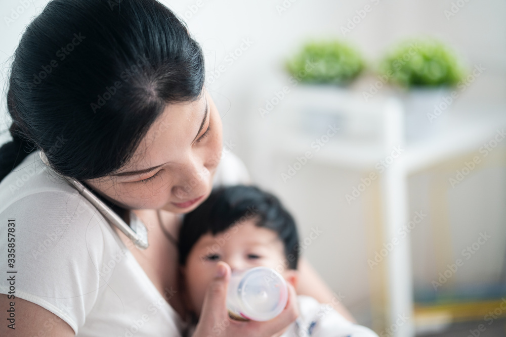 亚洲年轻忙碌的女人拥抱并给可爱的男婴喂奶。儿子很乐意呆在妈妈身边睡觉