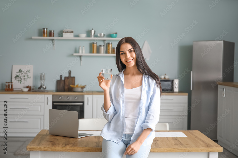 Beautiful young woman drinking water in kitchen