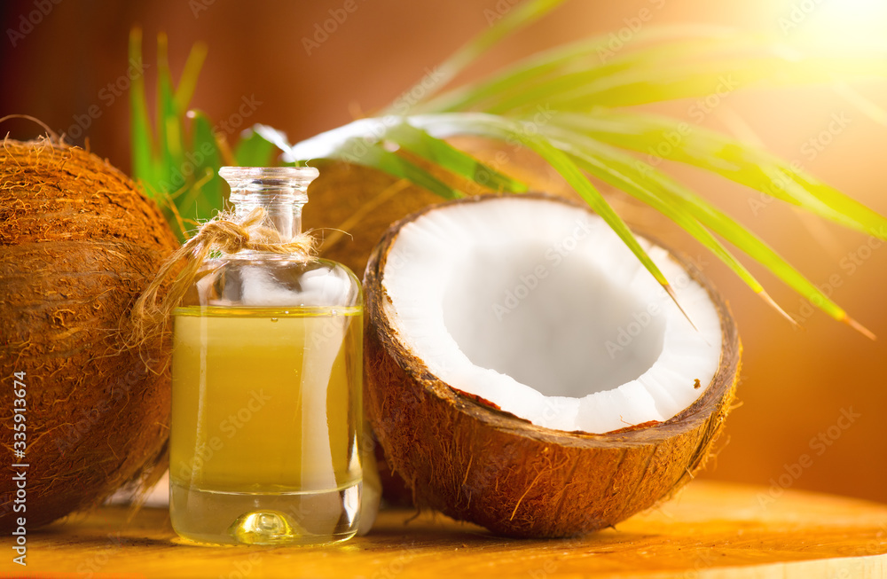 Coconut palm oil in a bottle with coconuts and green palm tree leaf on brown background. Coco nut cl