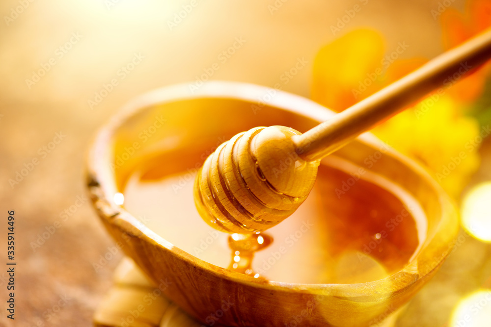 Honey dripping from honey dipper in wooden bowl.  Close-up. Healthy organic Thick honey dipping from