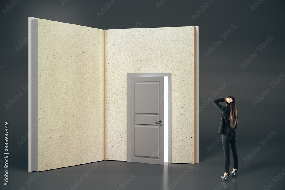 Pensive businesswoman looking at abstract open book with door on gray background.