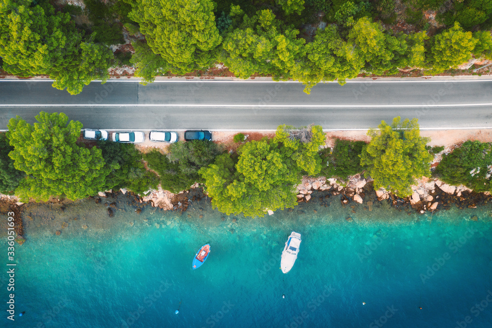 夏季日落时，美丽的绿色森林中的道路和海上的船只和游艇的鸟瞰图。Co