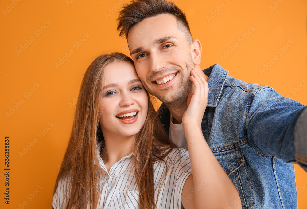 Happy young couple taking selfie on color background