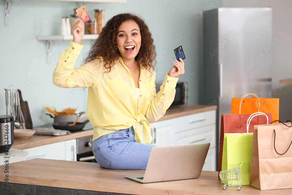 Happy woman with laptop, credit cards and shopping bags at home