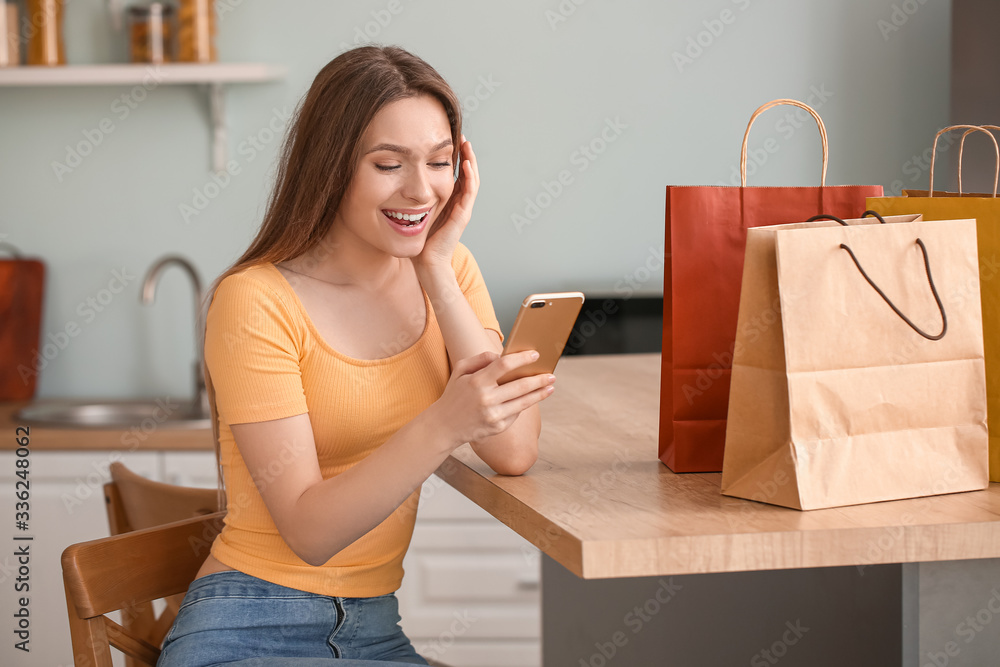 Young woman with mobile phone and shopping bags at home