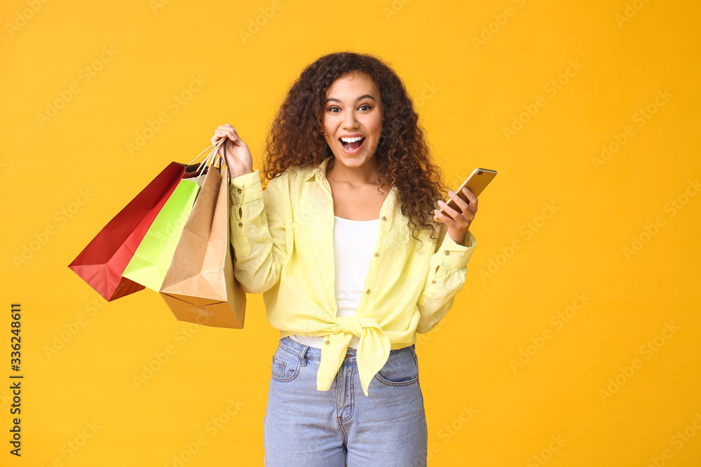 Happy woman with mobile phone and shopping bags on color background