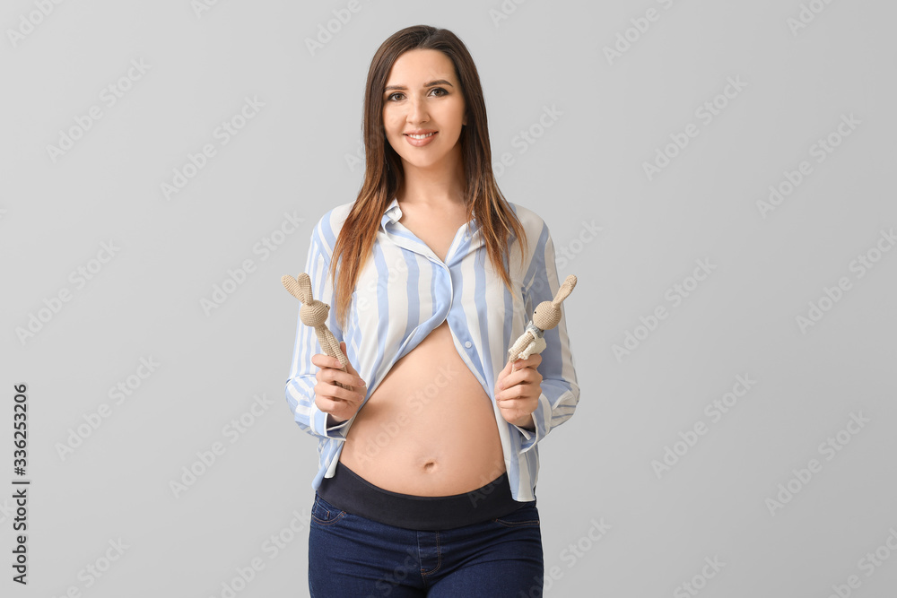 Beautiful pregnant woman with toys on grey background