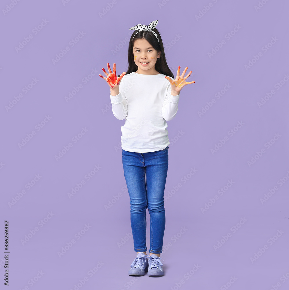 Cute little Asian girl with hands in paint on color background