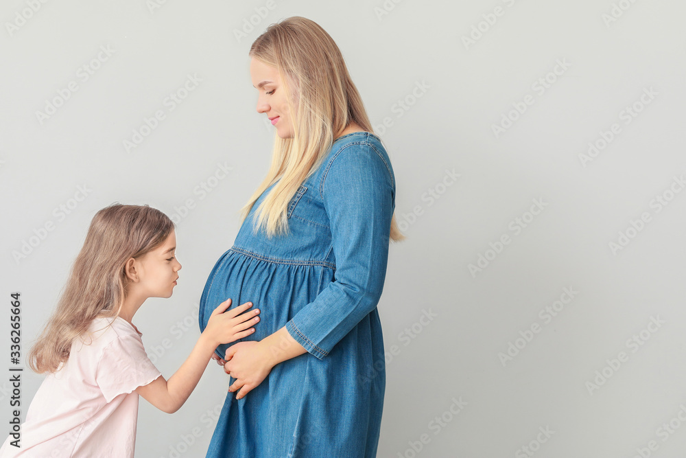 美丽的孕妇和她的小女儿在浅色背景下