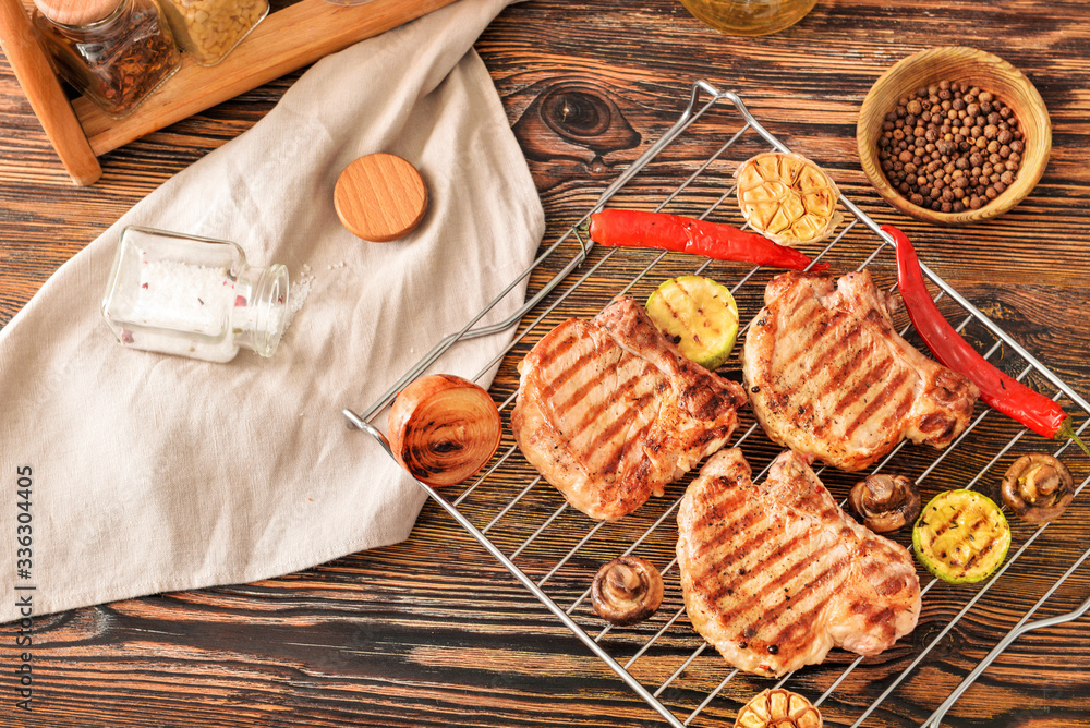 Rack with cooked pork steaks and vegetables on table