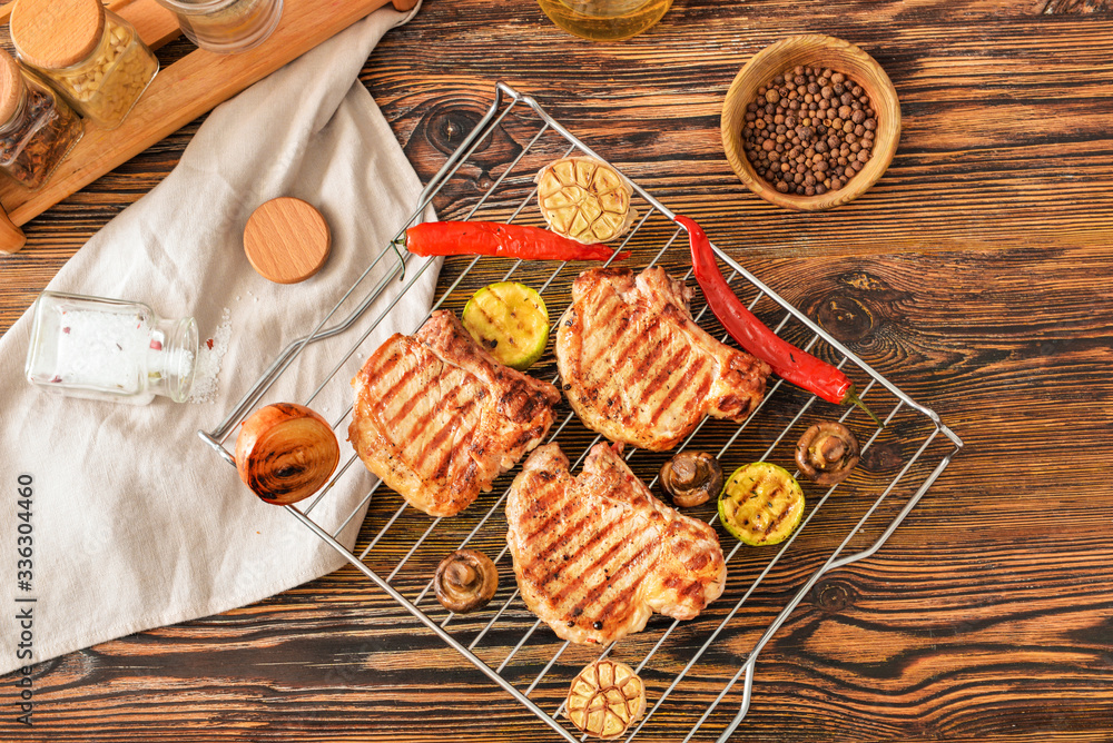 Rack with cooked pork steaks and vegetables on table