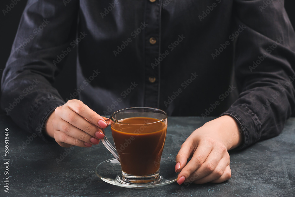 深色背景下拿着一杯冷咖啡的女人