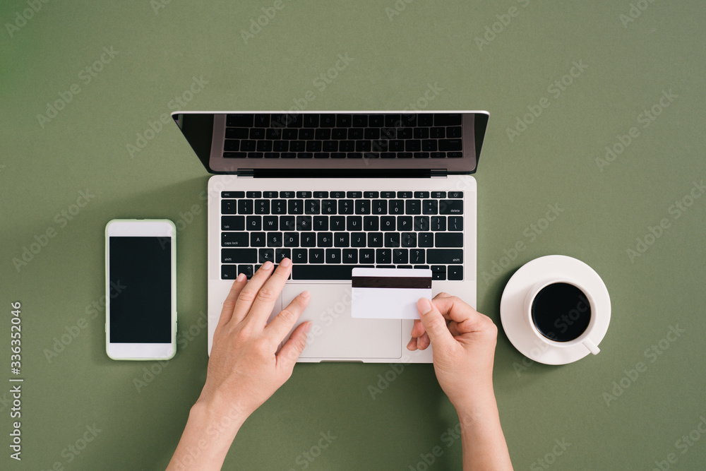 Woman using credit card with mobile phone and laptop and coffee cup on office desk. Online payment C