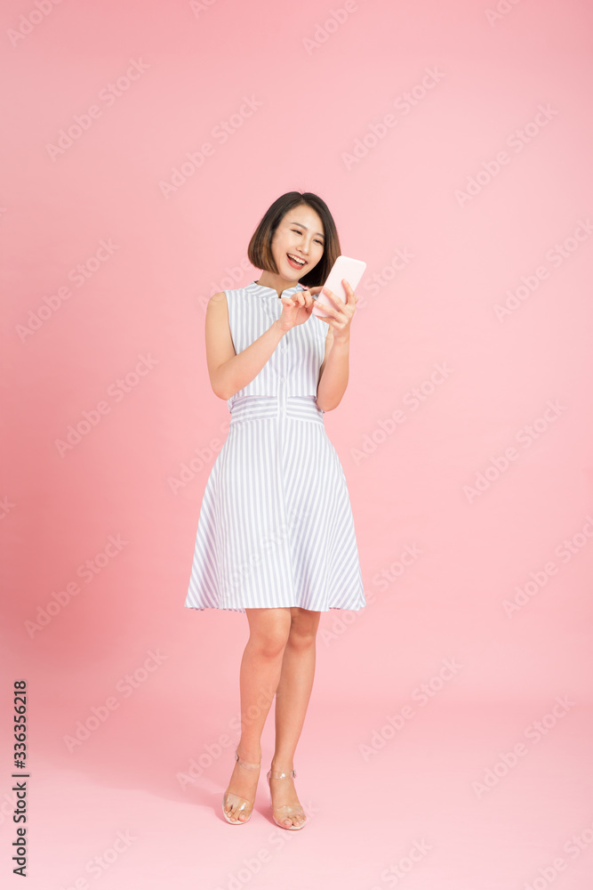 Full length portrait of a smiling casual girl using mobile phone isolated over pink background