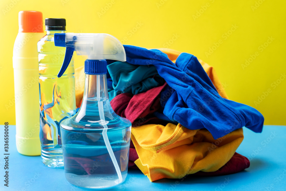 Plastic bottles of cleaning products set with pile clothes on blue table Yellow background.