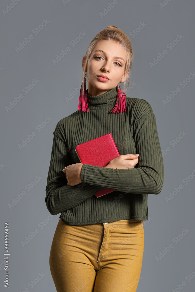 Young woman in warm sweater and with book on grey background