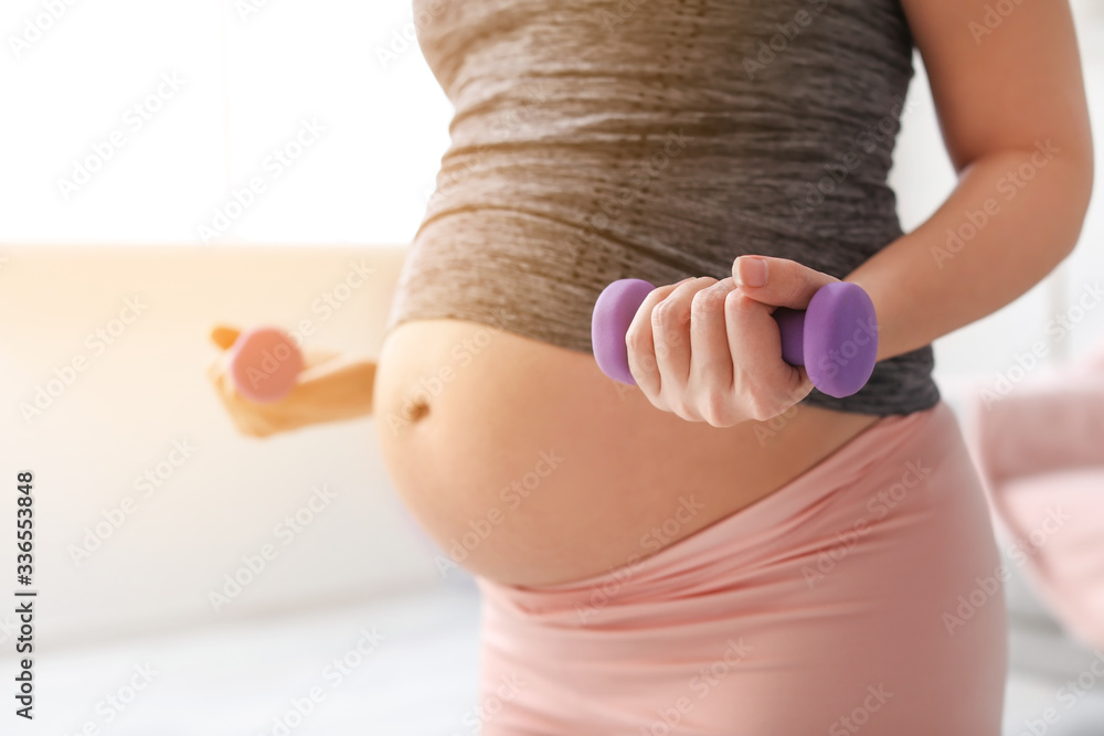 Beautiful sporty pregnant woman training with dumbbells at home, closeup