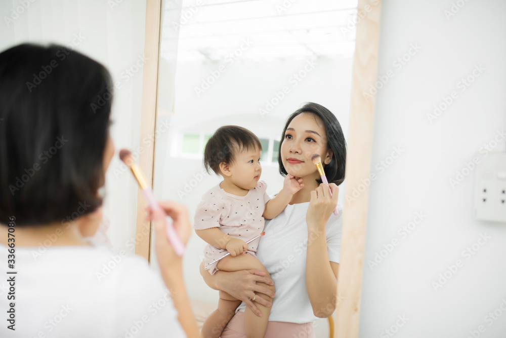 家里有个有趣的家庭。妈妈和她的小女儿正在化妆，在镜子附近玩得很开心。巴