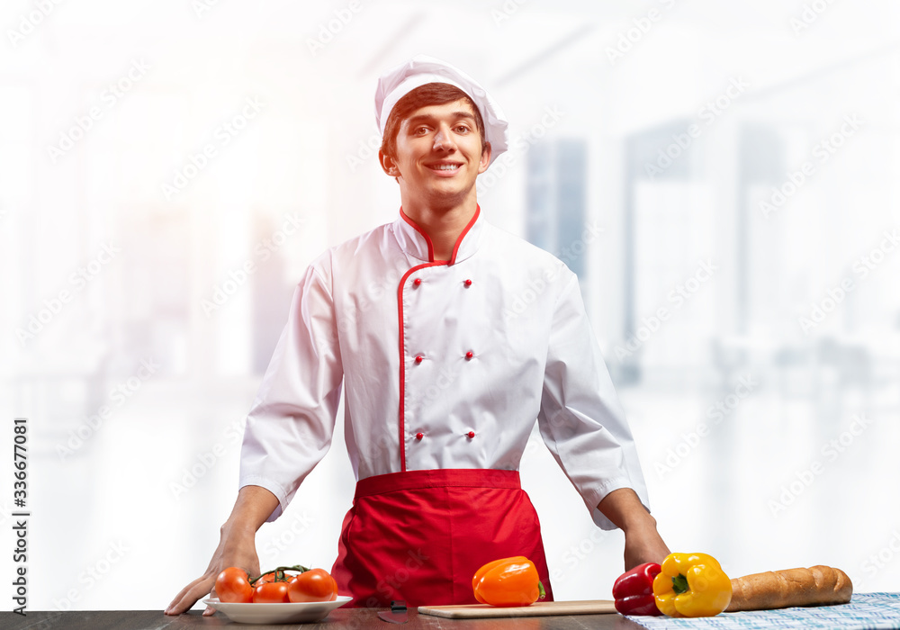 Young smiling chef standing near cooking table