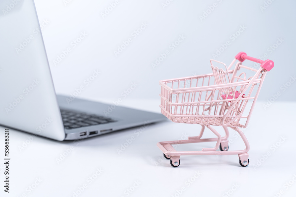 Online shopping. Mini empty pink shop cart trolley over a laptop computer on white table background,