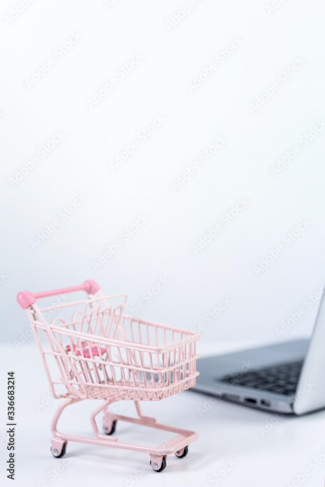 Online shopping. Mini empty pink shop cart trolley over a laptop computer on white table background,