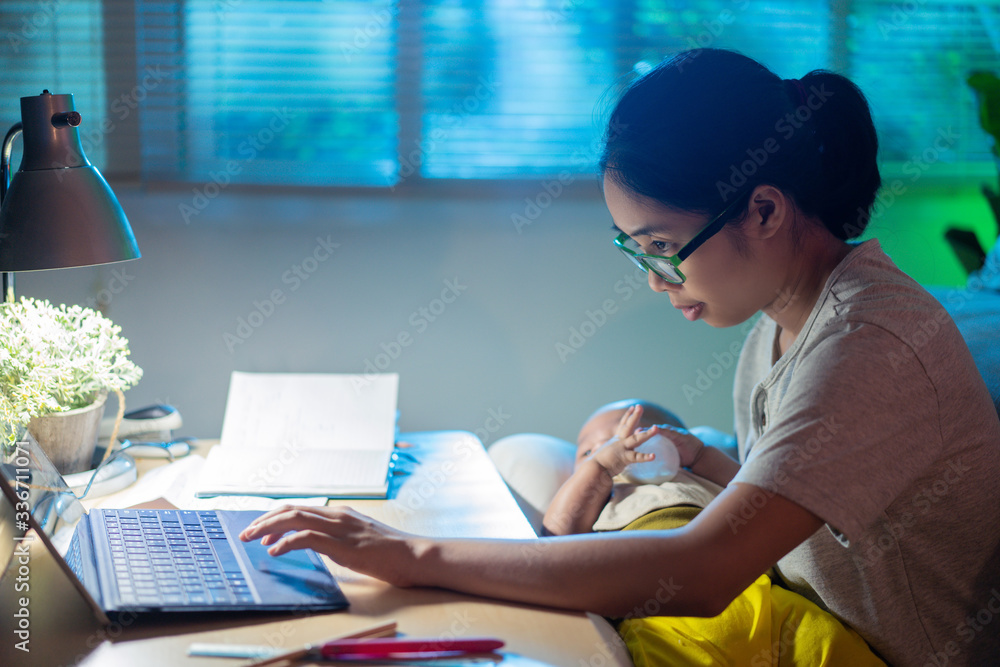 Asian mother and child Sitting and working at home at night, the mother is feeding the baby.