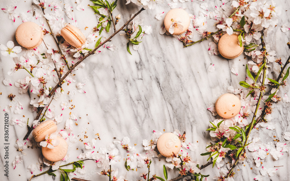 Flat-lay of sweet macaron cookies and white spring blossom flowers over white marble background, top