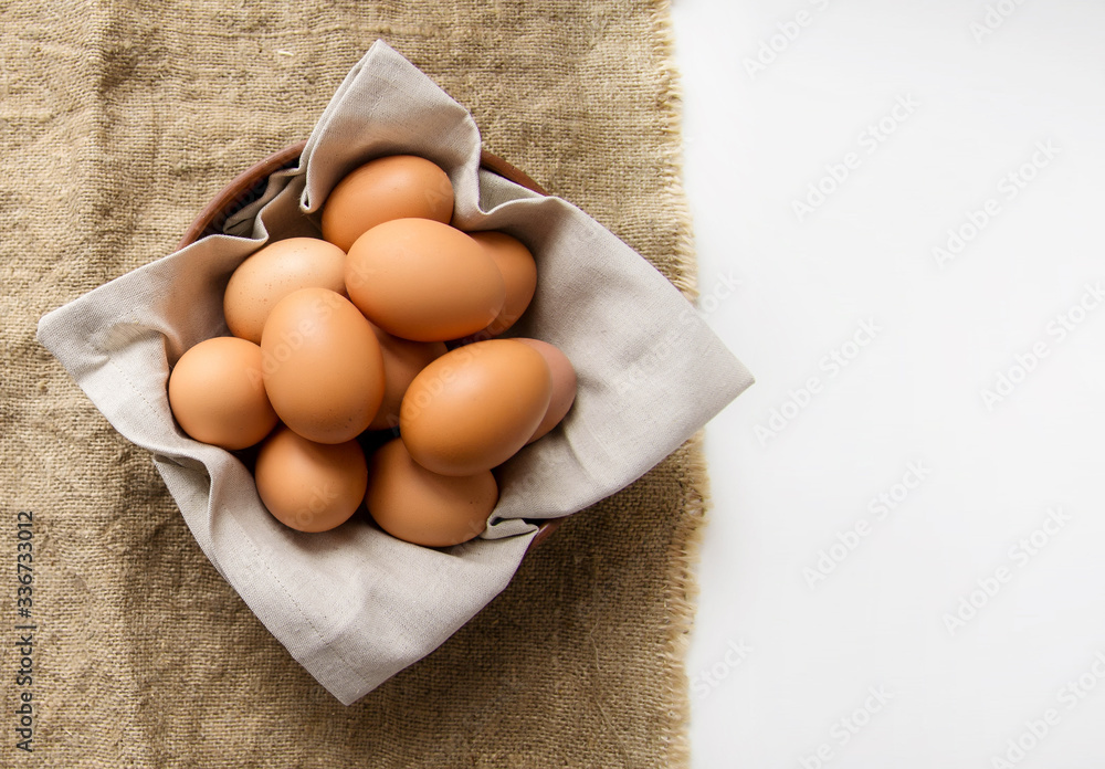 Chicken eggs in a clay plate with a linen napkin on burlap. View from above. Copy space.