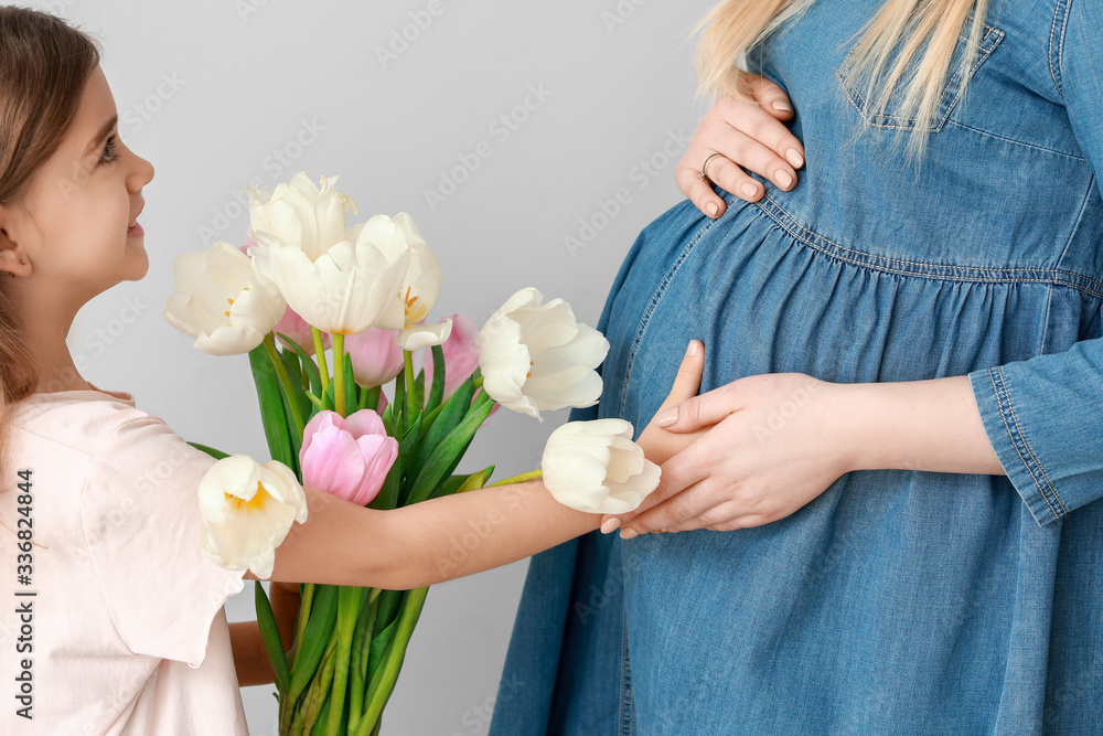 Little girl greeting her pregnant mother with flowers on light background