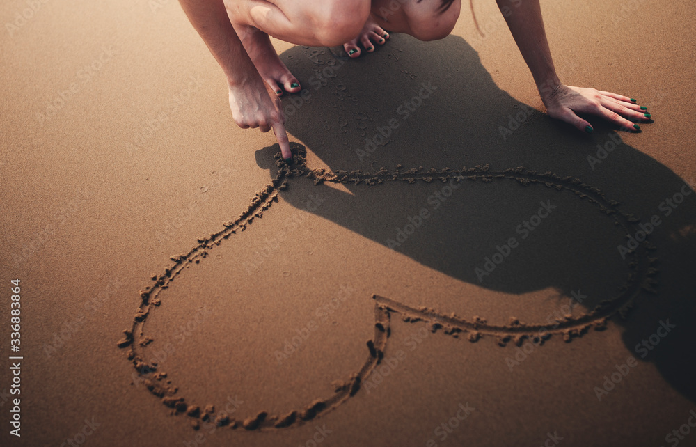 Closeup of hand drawing heart on sand