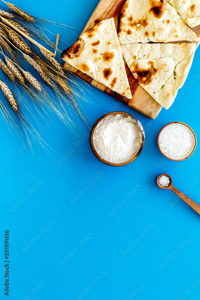 Focaccia ingredients. Wheat ears, flour, oil near bread on blue background top-down copy space