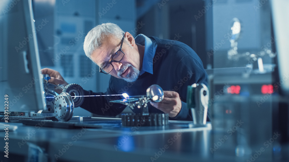 Portrait of Focused Middle Aged Engineer in Glasses Working with High Precision Laser Equipment, Usi