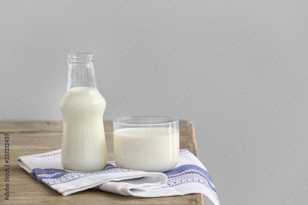 Glass and bottle of milk on table against grey background