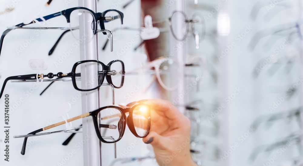 Selective focus on hand. Woman touching corrective glasses on stand with spectacles. Wide assortment