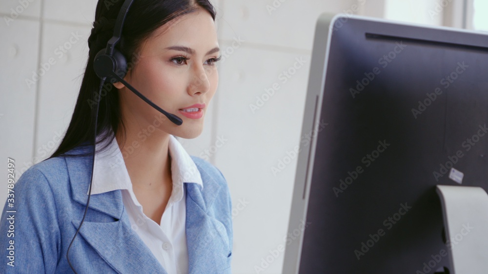 Customer support agent or call center with headset works on desktop computer while supporting the cu