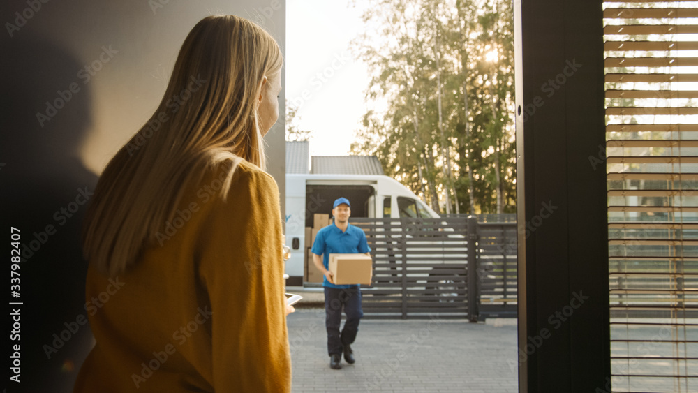 Delivery Man House and Delivers Cardboard Box Package to a Beautiful Young Woman. In the Background 