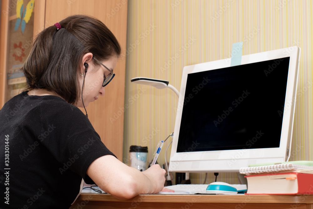 Closeup of a caucasian young woman writes in a notebook in front of a computer with a dark screen. D